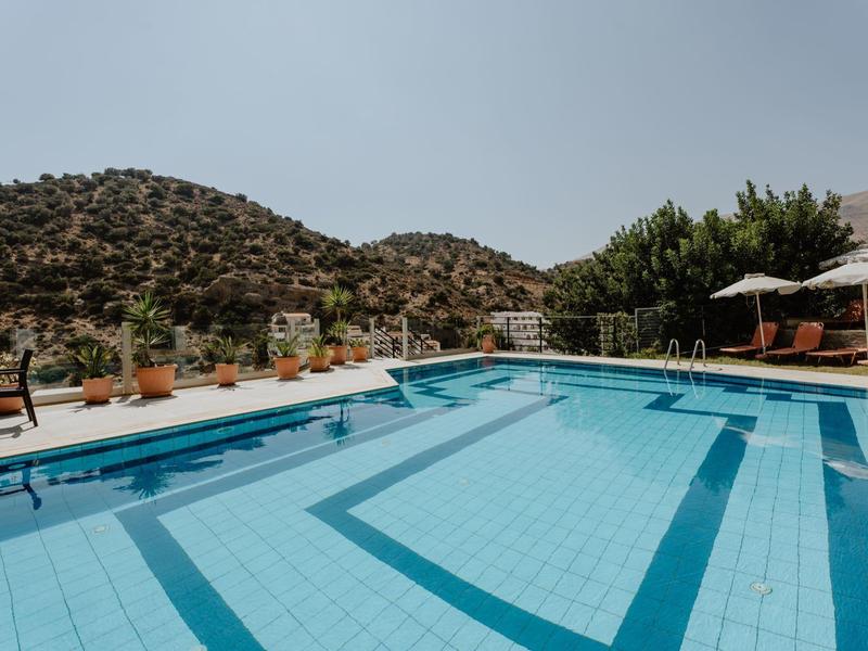 Venkovní bazén s výhledem na kopcovitou krajinu a posezením s deštníky.