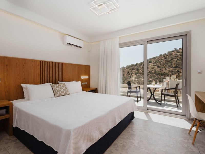 Světý hotelový pokoj s dvojlůžkem, dřevěným panelem, terasou a výhledem na hory.