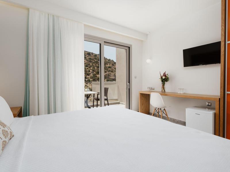 Světý hotelový pokoj s manželskou postelí, psacím stolem, televizí a přístupem na balkon.