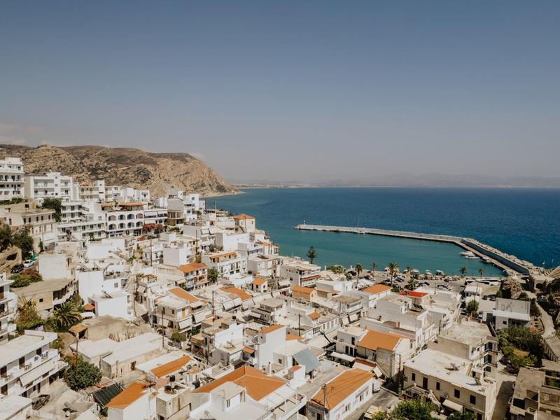 Pohled na pobřežní vesnici s bílými domy a přístavem u moře pod jasnou oblohou.