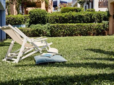 A deck chair with two cushions on a well-maintained lawn in front of green hedges.