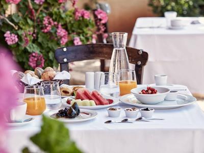Outdoor breakfast table with fresh fruit, juices, and dishes, surrounded by flowers.