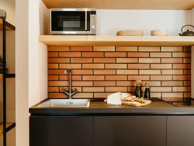 Modern kitchenette with microwave, sink, and kitchen utensils against brick wall.