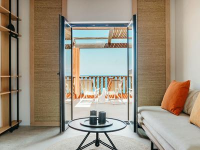 Modern living area with view of sunny terrace and sea through open glass door.