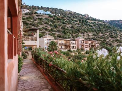 Path beside red buildings with green vegetation and hills in the background.