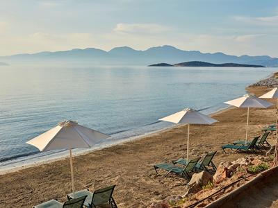 Spiaggia con lettini e ombrelloni sul mare calmo con montagne sullo sfondo.