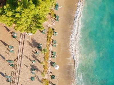 Aerial view of a sandy beach with umbrellas, sun loungers, and clear turquoise water.