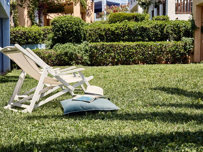 A deck chair with two cushions on a well-maintained lawn in front of green hedges.