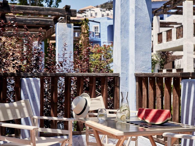 Balcony with wooden furniture, hat and book, surrounded by buildings and plants.