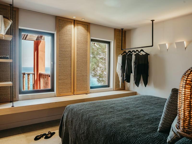 Modern bedroom with double bed, clothes rack, and two windows showing outdoor view.