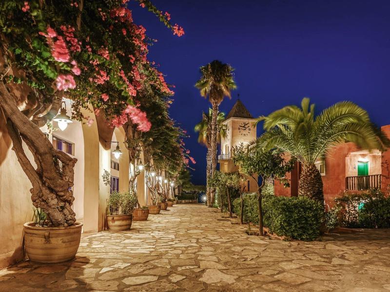Illuminated stone pathway with bougainvillea and palm trees at night in a hotel garden.