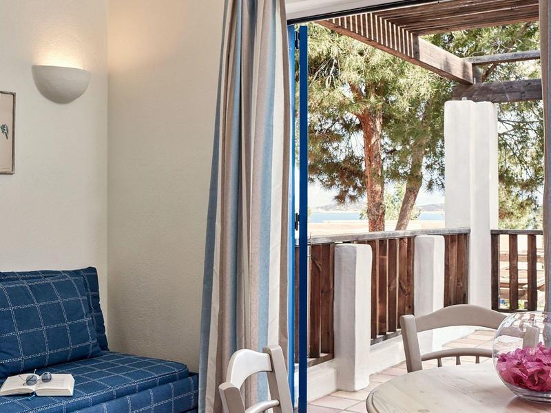 Cozy hotel room interior with blue sofa and balcony view of trees and wooden railing.