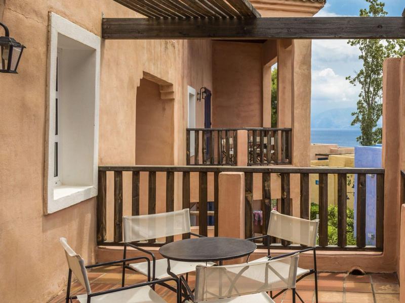 Balcony with table and four chairs, view of sky and nature, beige walls and brown wooden railing.