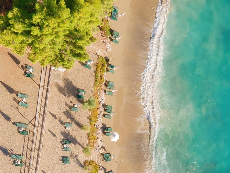 Aerial view of a sandy beach with umbrellas, sun loungers, and clear turquoise water.