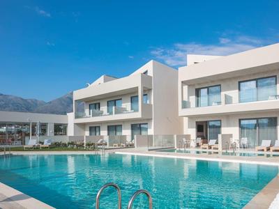 Nowoczesny kompleks hotelowy z basenem na zewnątrz, otoczony górami pod niebieskim niebem.