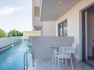 Nowoczesny balkon z widokiem na basen, biały stół i krzesła obok pokoju hotelowego.