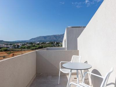 Balkon z białym stołem i krzesłami, widok na krajobraz i góry pod niebieskim niebem.