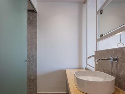 Nowoczesna łazienka z okrągłą umywalką i szarymi płytkami na ścianie.