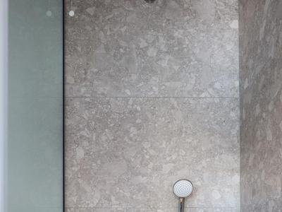 Nowoczesny prysznic z okrągłą deszczownicą i szarymi kafelkami na ścianie.