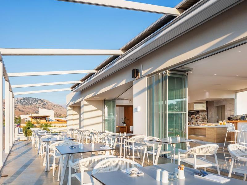 Otwarty taras z stołami i krzesłami obok nowoczesnej restauracji hotelowej w świetle dziennym.