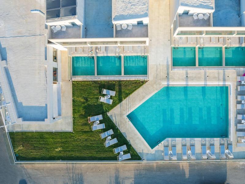 Widok z góry na basen hotelowy z leżakami i trawnikiem.