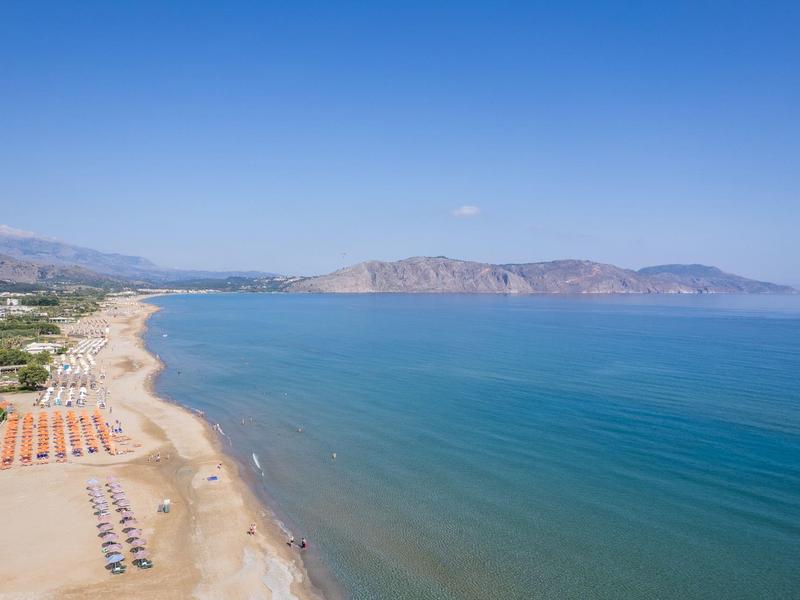 Długa piaszczysta plaża z parasolami i błękitnym morzem pod czystym niebem.