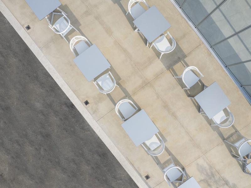 Widok z lotu ptaka na taras z białymi stołami i krzesłami wzdłuż budynku.