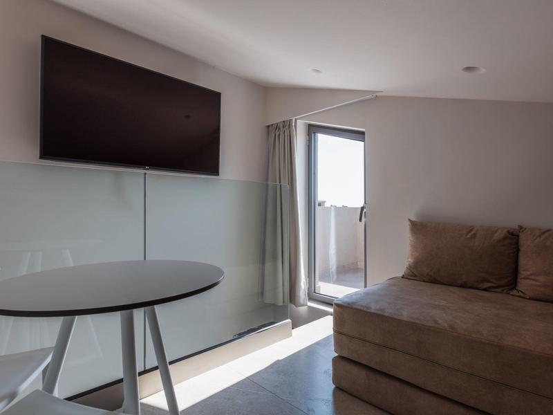 Nowoczesny pokój hotelowy z sofą, małym stolikiem i balkonem w tle.