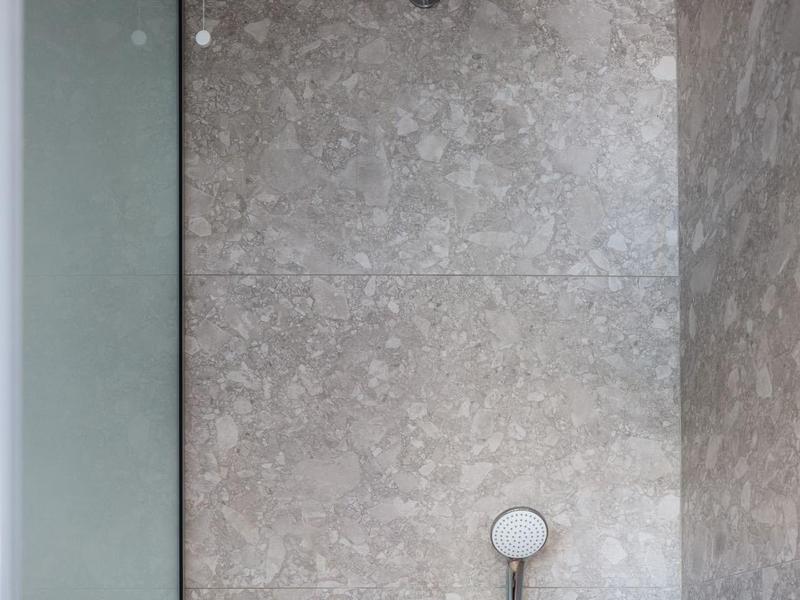 Nowoczesny prysznic z okrągłą deszczownicą i szarymi kafelkami na ścianie.