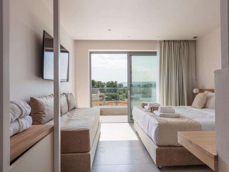 Nowoczesny pokój hotelowy z łóżkiem, sofą, telewizorem i balkonem z widokiem na morze.