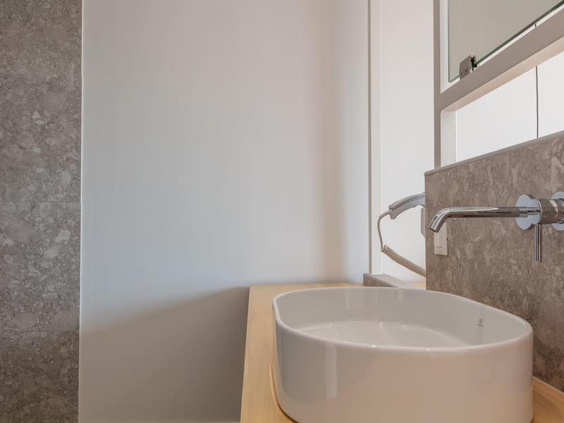 Nowoczesna łazienka z okrągłą umywalką i baterią ścienną w neutralnych kolorach.