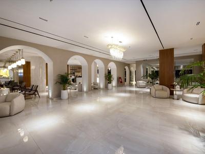 Prostorná hotelová hala s moderním osvětlením, bílými podlahami a pohodlnými posezeními s rostlinami.