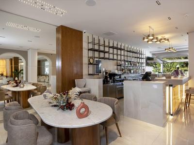 Moderní hotelová jídelna s mramorovými stoly, čalouněnými židlemi, barem a dekorativním osvětlením.