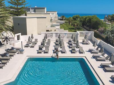 Moderner Swimmingpool mit Liegestühlen und Sonnenschirmen auf einer Hotelterrasse mit Meerblick.