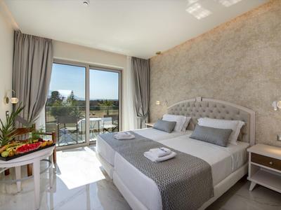 Světý hotelový pokoj s manželskou postelí, šedým dekorem, balkonem a venkovním výhledem.