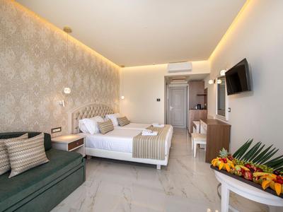 Camera d'hotel moderna con letto matrimoniale, divano, TV e composizione floreale decorativa.