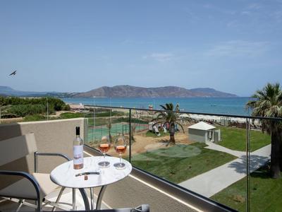 Balcone con tavolo e sedie con vista su giardino, mare e montagne sotto cielo sereno.