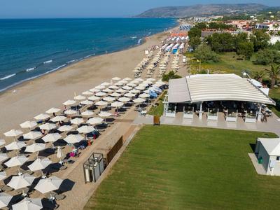 Lunga spiaggia sabbiosa con file di ombrelloni e un ristorante sulla spiaggia accanto a un prato verde.