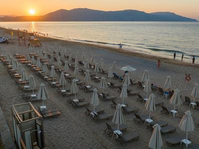Spiaggia con file di ombrelloni chiusi e mare calmo al tramonto.