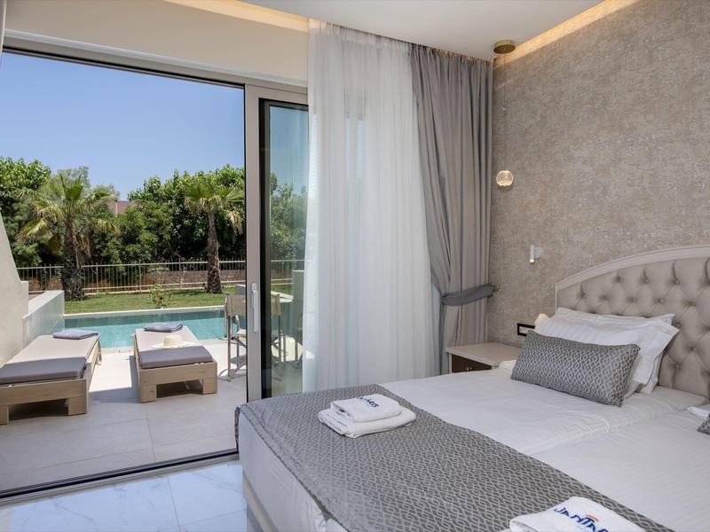 Pohodlná ložnice se šedým dekorem a výhledem na bazén přes otevřené posuvné dveře.