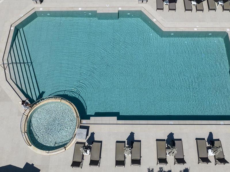 Pohled shora na venkovní bazén s lehátky a slunečníky na terase.