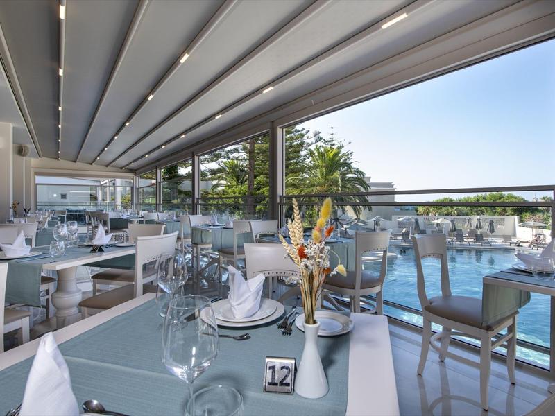 Moderní venkovní jídelní prostor se skleněnými stoly a výhledem na bazén.