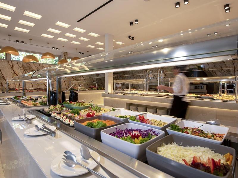 Bufet s čerstvými saláty a přílohami v jasné jídelně hotelu.