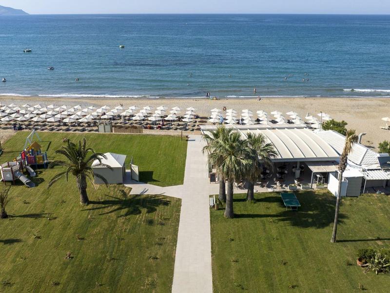 Přímořské letovisko s lehátky, slunečníky, palmami a jasným výhledem na oceán.