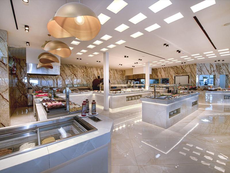 Prostorná moderní bufetová místnost s mramorovými stěnami, velkými závěsnými světly a elegantními stanovišti.