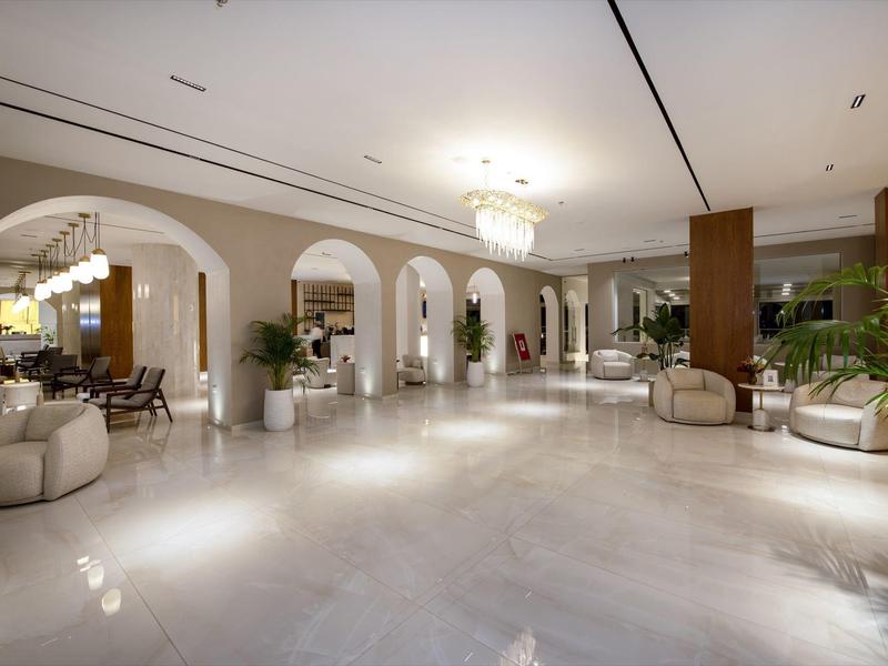 Prostorná hotelová hala s moderním osvětlením, bílými podlahami a pohodlnými posezeními s rostlinami.