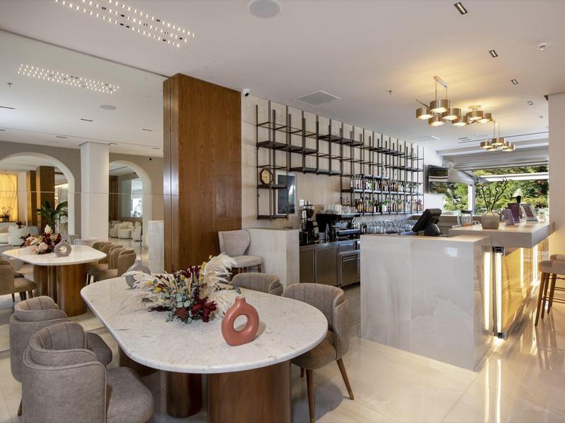 Moderní hotelová jídelna s mramorovými stoly, čalouněnými židlemi, barem a dekorativním osvětlením.