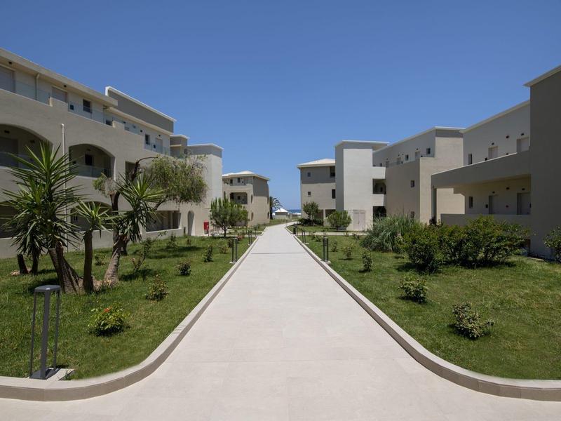 Cesta mezi moderními bílými hotelovými budovami s zelenými zahradami a jasnou modrou oblohou