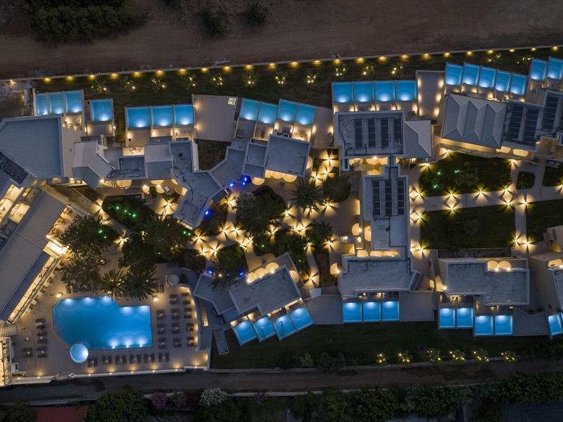 Letecký pohled na resort v noci s osvětlenými budovami a zářícím bazénem.