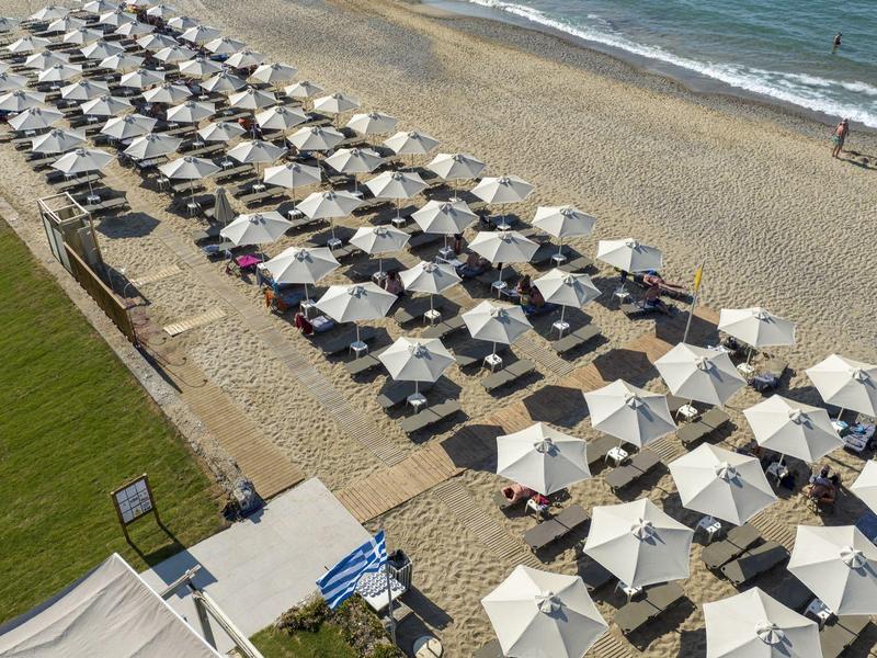 Řady bílých plážových slunečníků a lehátek na písečné pláži u oceánu.